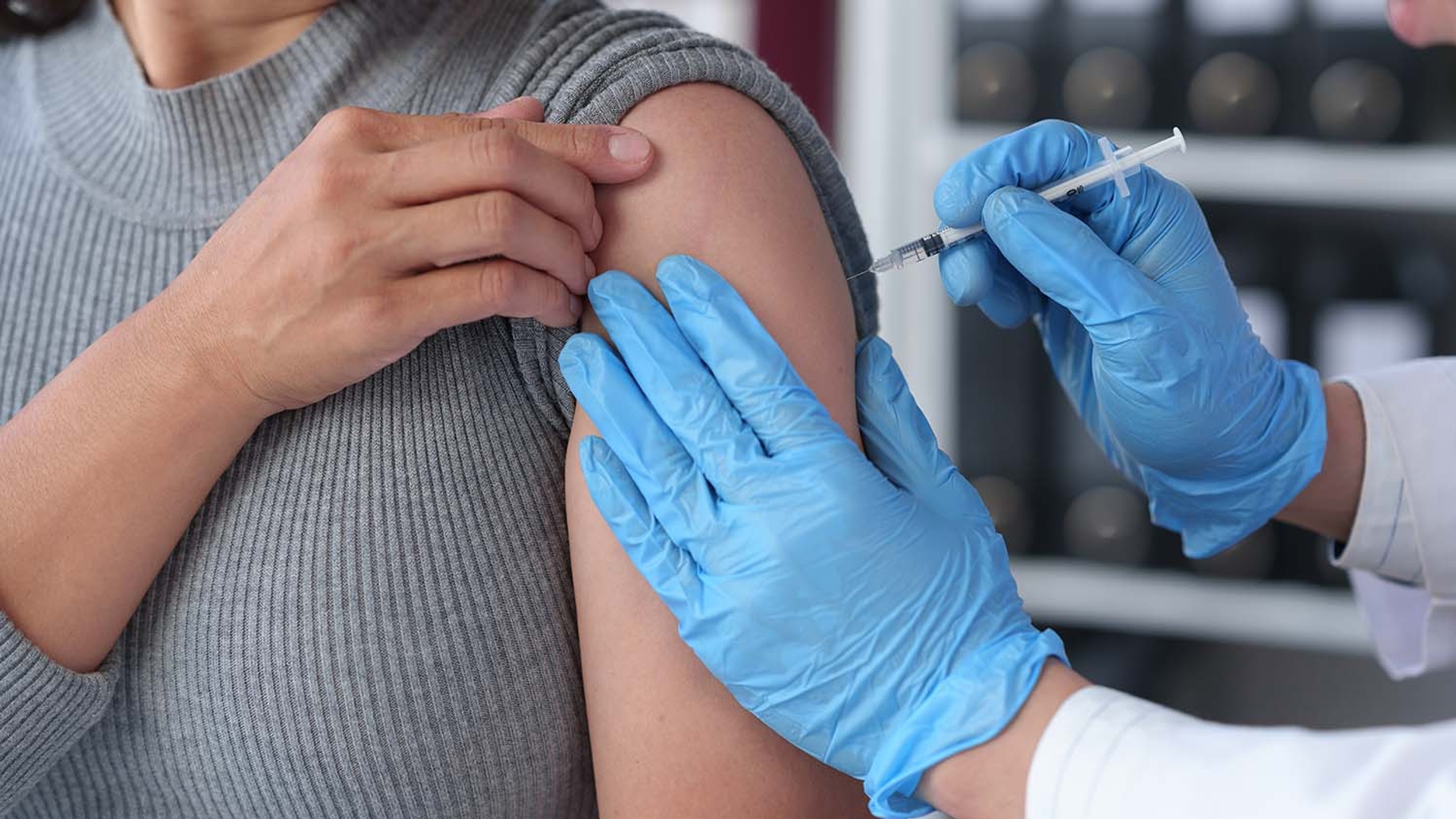 Healthcare professional administering a vaccine to a patient's arm in a clinical setting.