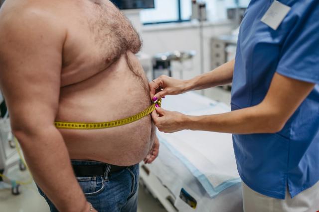 A healthcare worker measures the prominent belly of a man with a tape measure.