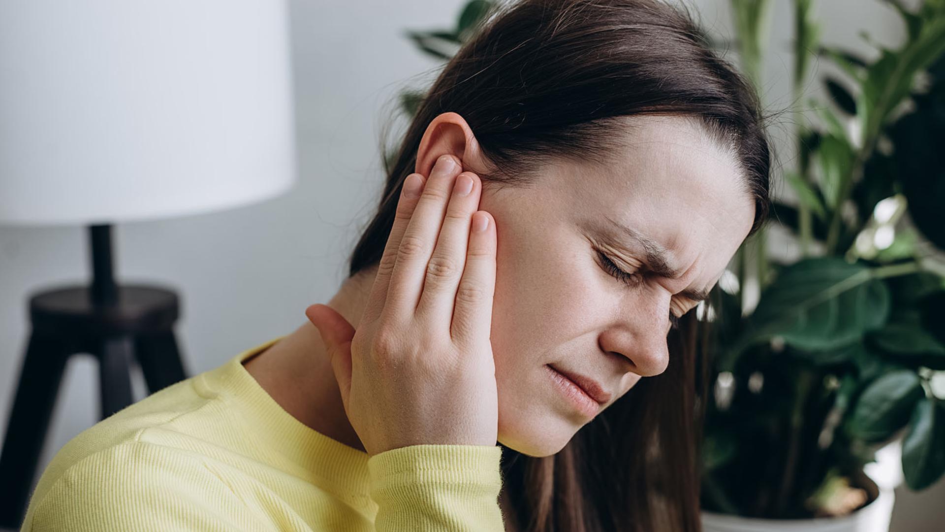 A woman grimaces in pain while holding her ear.