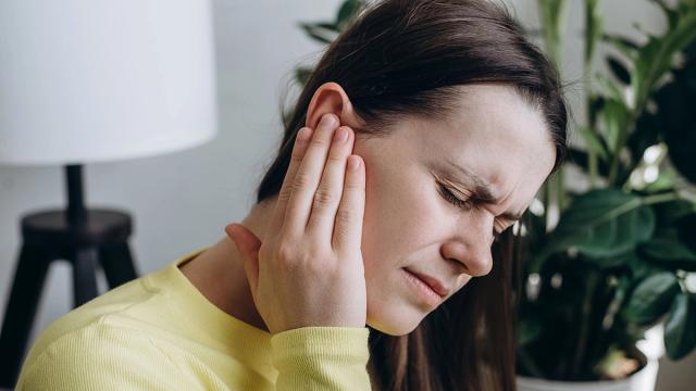A woman grimaces in pain while holding her ear.