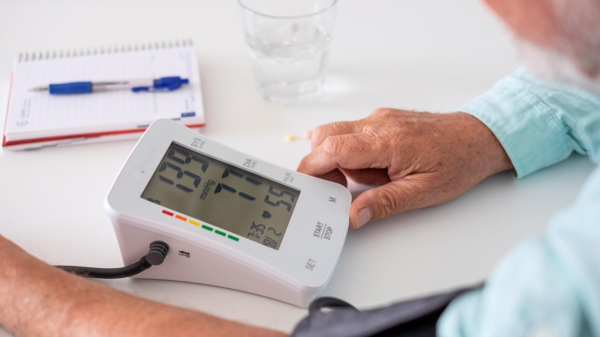 An older person takes their blood pressure with a digital monitor displaying 137/77 mmHg.