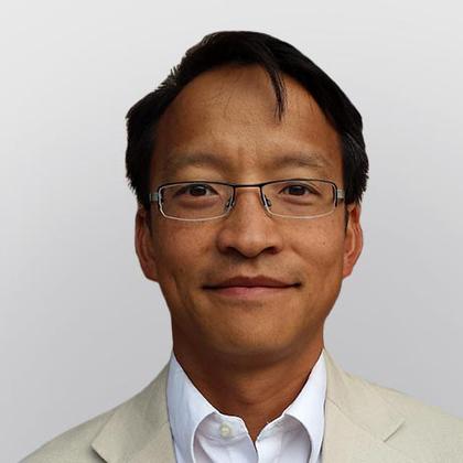 Middle-aged Asian man wearing glasses and a beige blazer over a white shirt, against a light gray background.