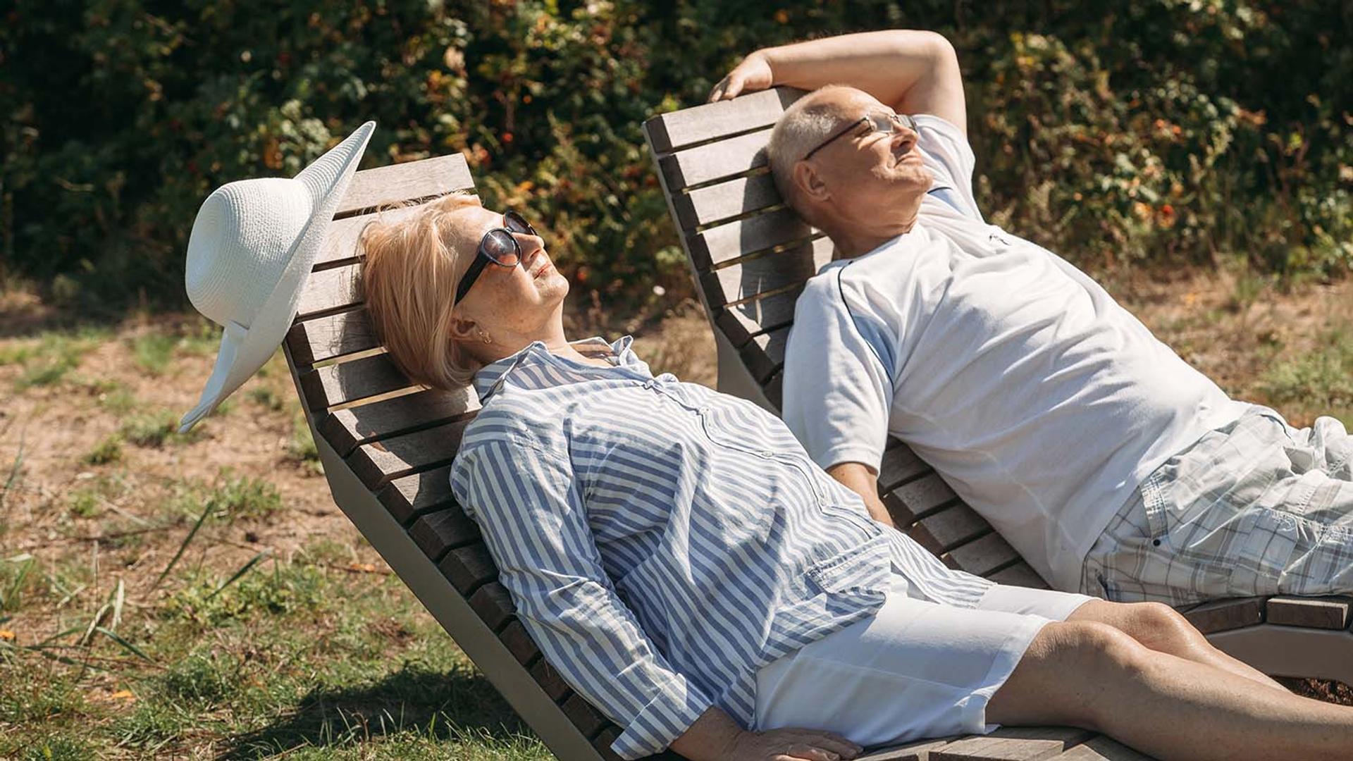 Elderly couple relaxing on sun loungers outdoors.