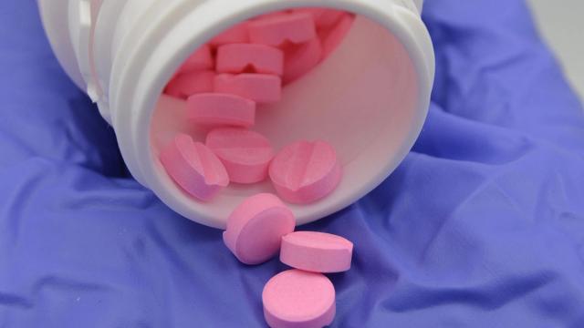 Pink pills spilling from a white bottle onto a purple gloved hand.