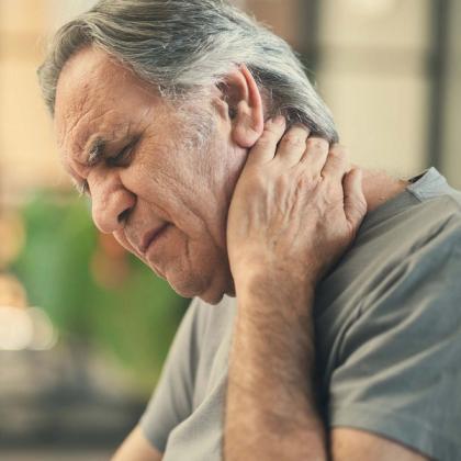 An older man with grey hair holds his neck with one hand, his eyes closed in pain.