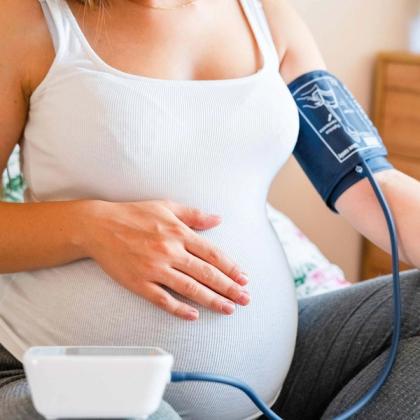 A pregnant woman with a blood pressure cuff on her arm and her hand resting on her belly.