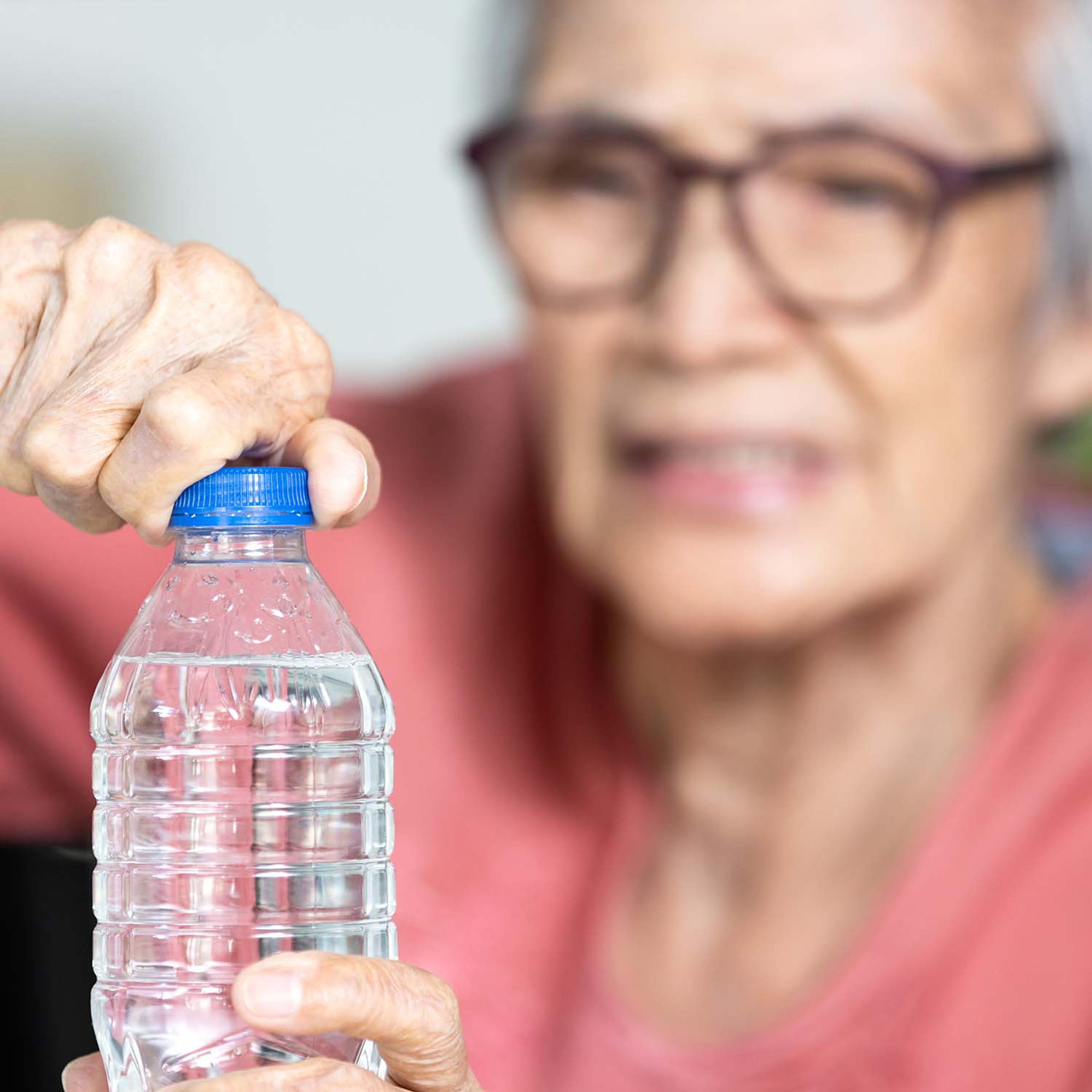 An elderly person's hands struggle to open a water bottle, with their blurred face showing effort.