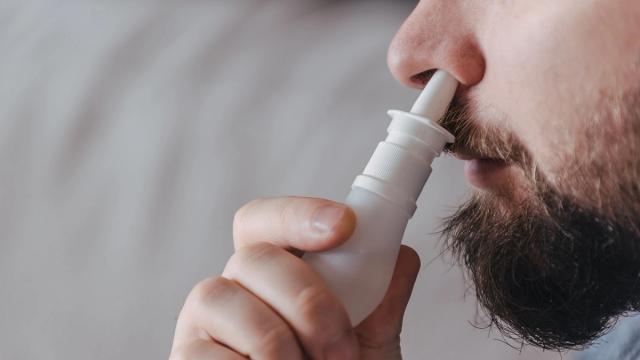 Close-up of a bearded man using a nasal spray.
