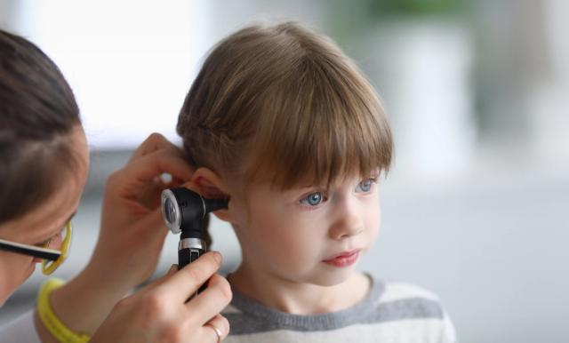 A doctor examines a young child's ear with an otoscope.