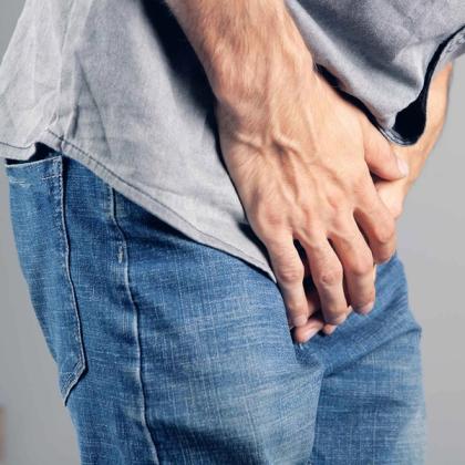 Close-up of a man in jeans grasping his lower back in pain, indicating discomfort or a backache.