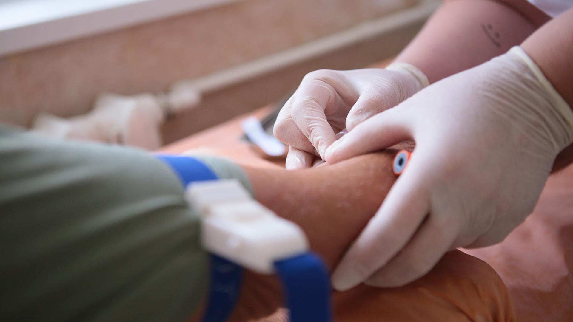 Gloved hands inserting an IV into an arm with a tourniquet.