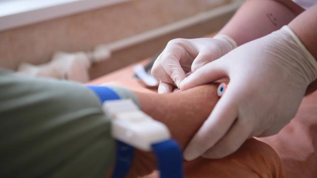 Gloved hands inserting an IV into an arm with a tourniquet.
