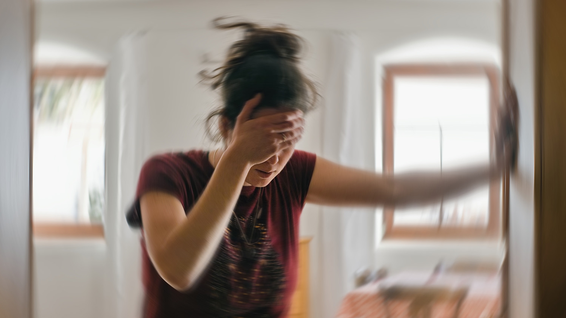 Woman in distress with blurred motion, covering her face with one hand in a brightly lit indoor setting.