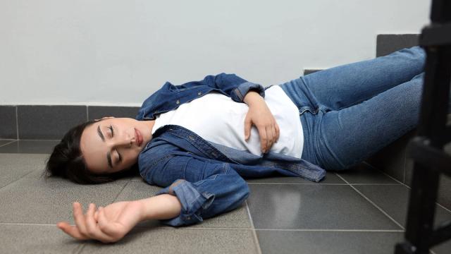 Unconscious woman lying on a tiled floor at the base of stairs.