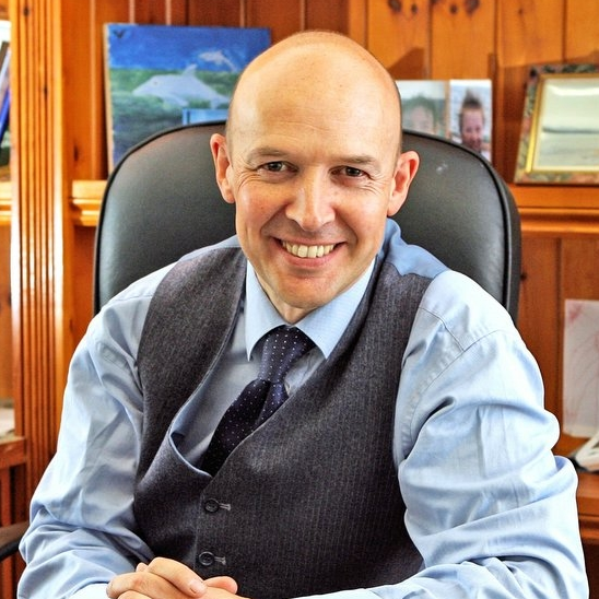 Bald businessman smiling in office, wearing blue shirt and gray vest