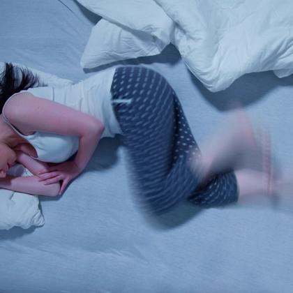 Woman in pajamas experiencing restless legs syndrome while lying in bed