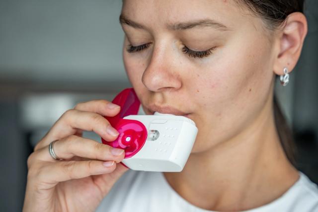 A woman uses a white and pink inhaler.