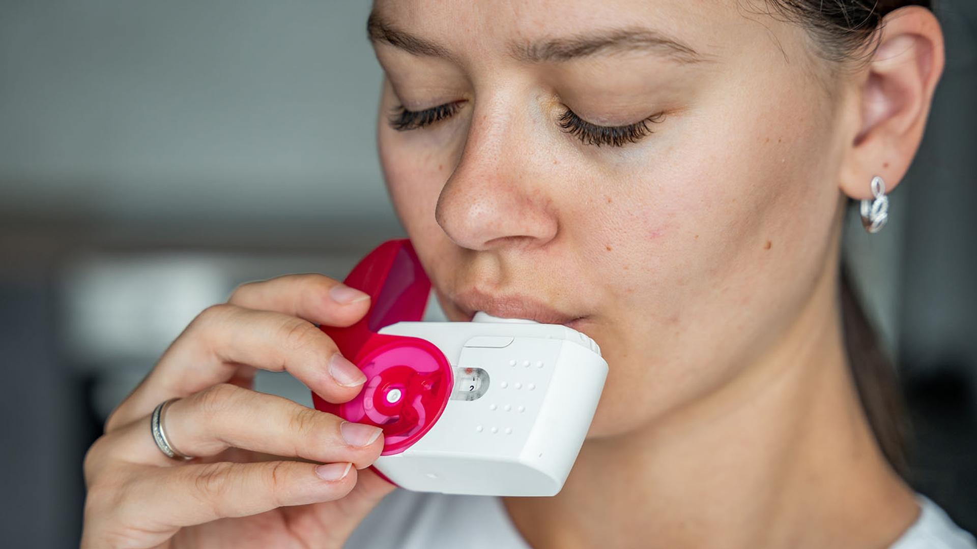A woman with closed eyes uses a white and pink inhaler.