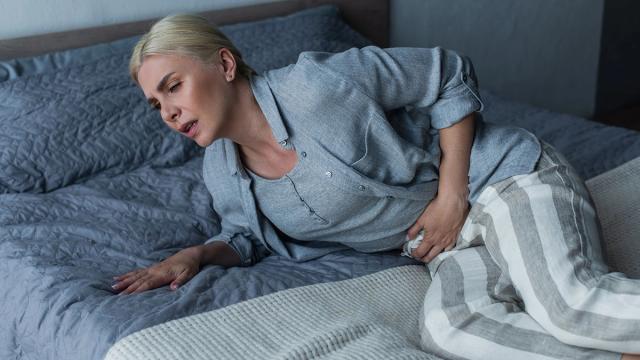A woman lying on a bed, grimacing and clutching her stomach in pain.