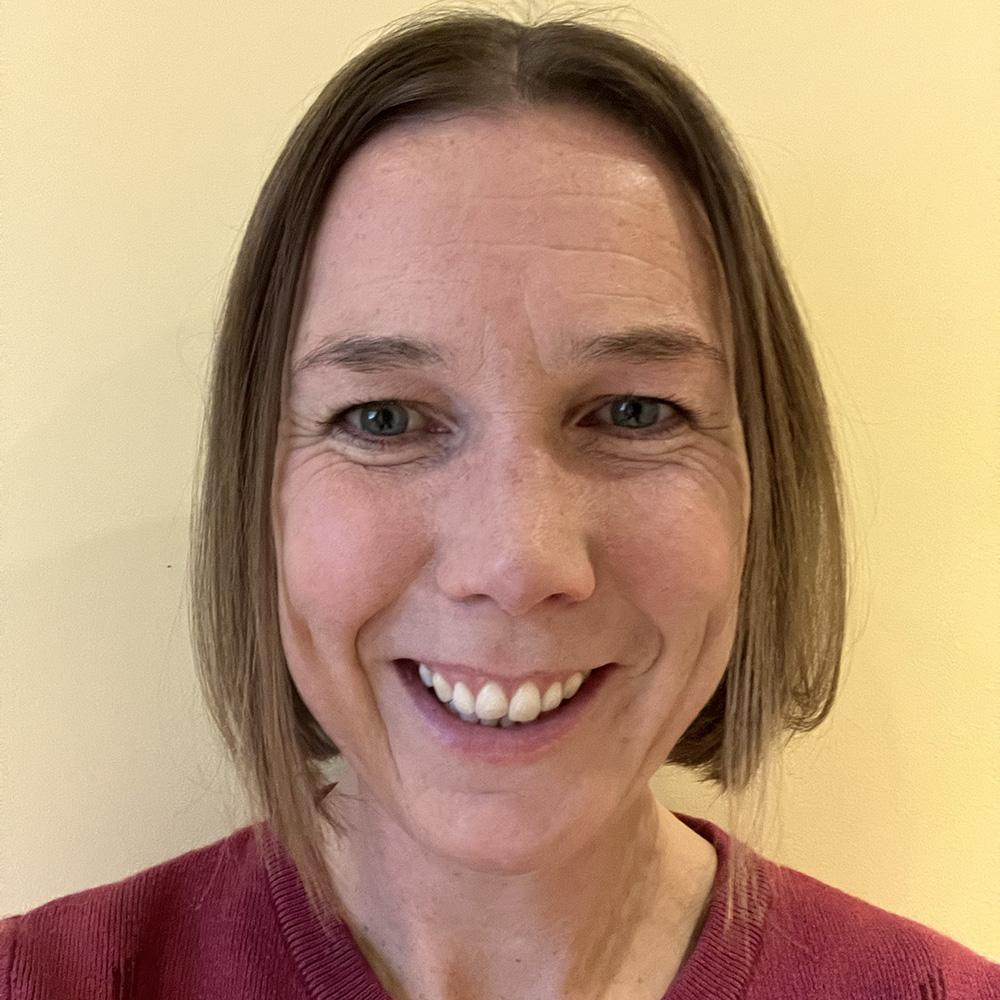 Close-up portrait of a smiling woman with shoulder-length brown hair wearing a red sweater.
