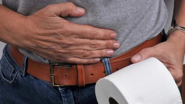 A person clutches their stomach while holding a roll of toilet paper.