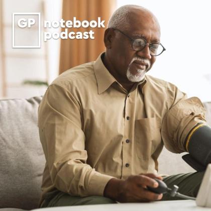 Senior African American man recording a podcast, wearing glasses and beige shirt, with microphone and laptop on table.
