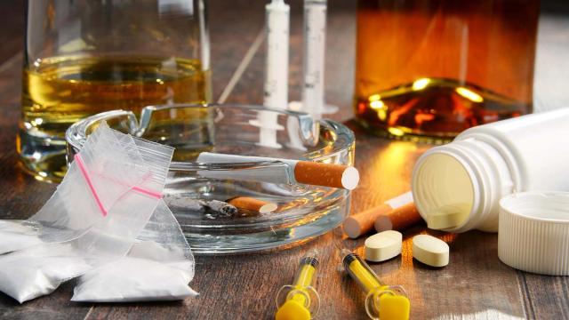 Illegal drugs, alcohol, tobacco, syringes, and prescription pills on a table.