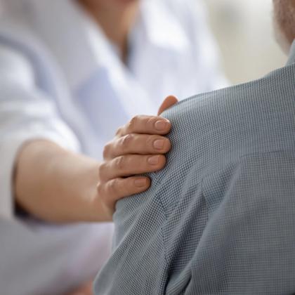 Close-up of a healthcare professional's hand gently placed on a patient's shoulder in a reassuring manner.