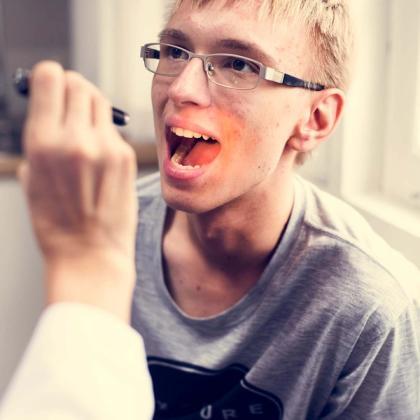 A doctor shines a light into a young man's open mouth during an examination.