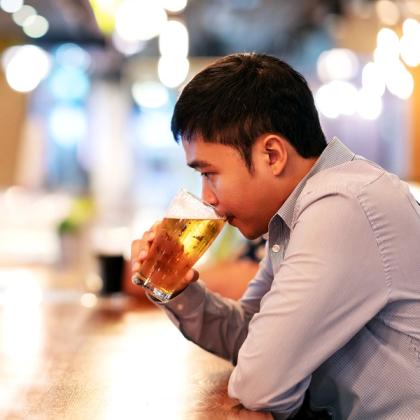 Young man drinking a glass of beer in a bar with blurred lights in the background