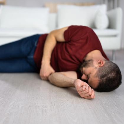 Man lying on the floor in fetal position with distressed expression, in a minimalist living room setting.