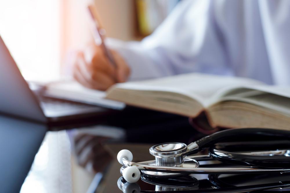 Doctor taking notes with a book open and a stethoscope in the foreground