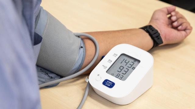 A person's arm with a blood pressure cuff and a digital monitor showing 143/93 and pulse 83.