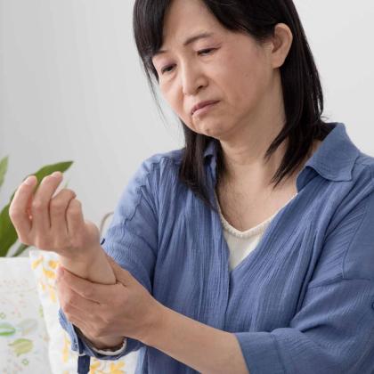 Middle-aged woman with a pained expression holding her wrist, possibly experiencing joint pain or discomfort.