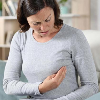 Woman in gray top looking at her arm with a concerned expression, possibly experiencing arm pain or discomfort.