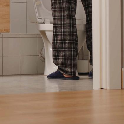 Person in plaid pajamas and slippers standing at a toilet in a bathroom