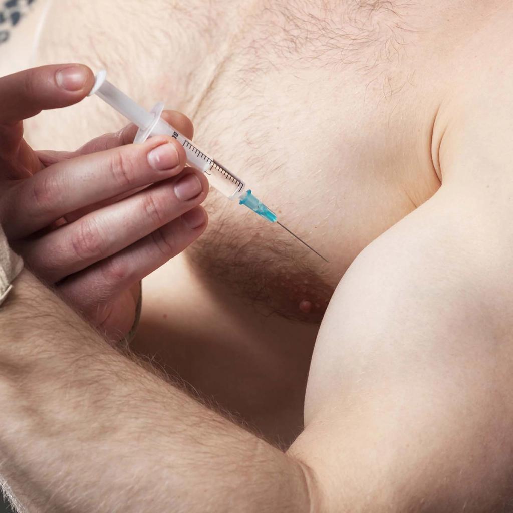 A hand holding a syringe with the needle poised to inject into a muscular upper arm.