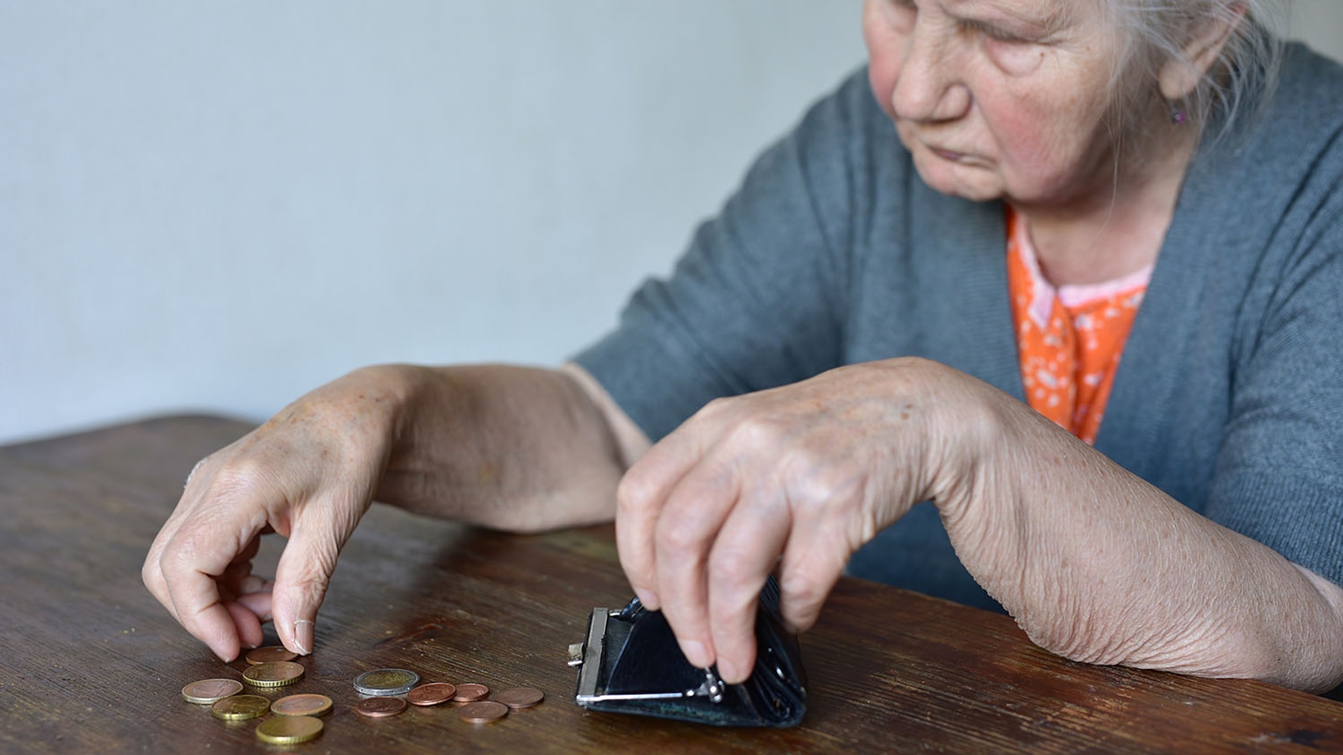 Elderly person counting a few coins next to an open, empty coin purse on a wooden table.