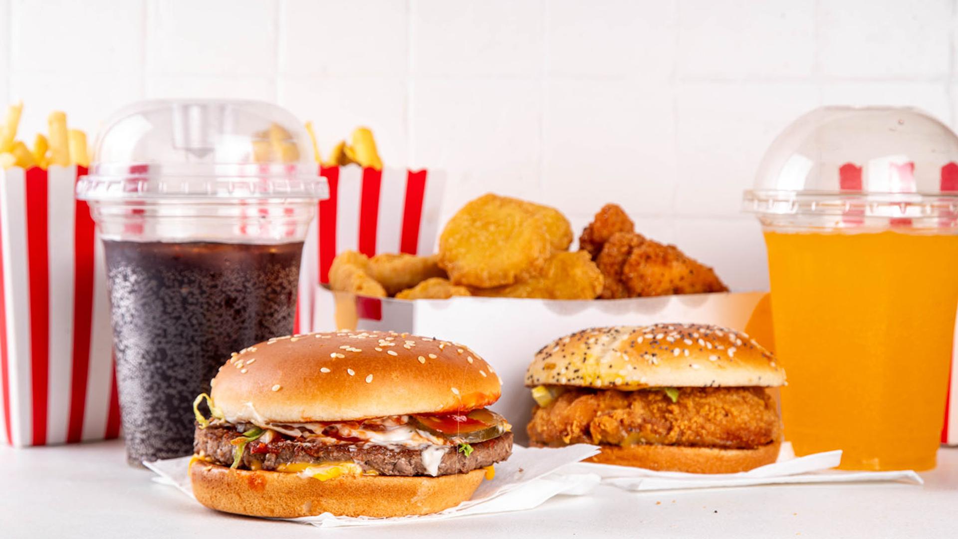 Assorted fast food: cheeseburger, fried chicken sandwich, fries, chicken nuggets, cola, and orange drink.