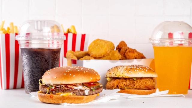 Assorted fast food: cheeseburger, fried chicken sandwich, fries, chicken nuggets, cola, and orange drink.