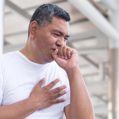 Middle-aged man coughing into his fist, appearing distressed, with one hand on his chest