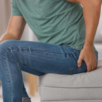 Close-up of a person wearing blue jeans seated on a gray ottoman, focusing on the midsection with a hand on the hip.