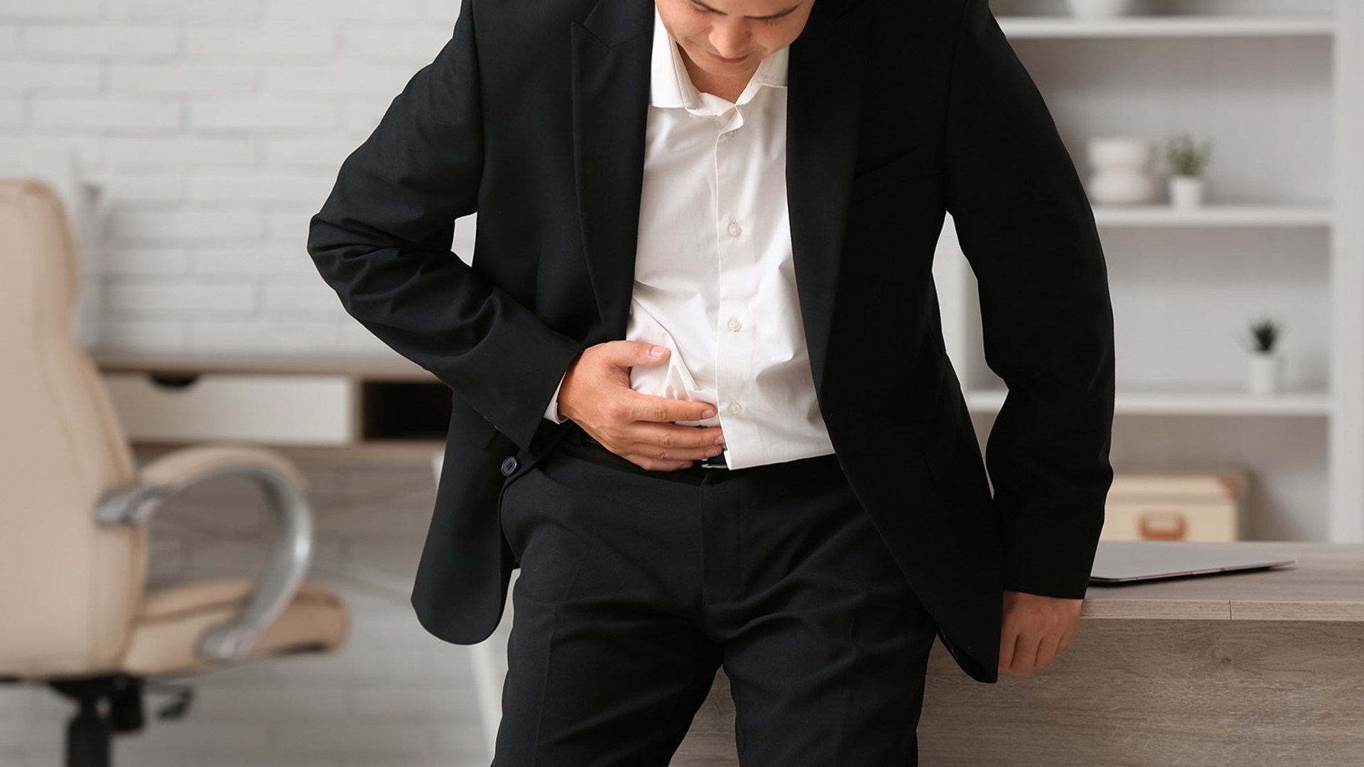 A man in a suit holds his stomach, looking uncomfortable.