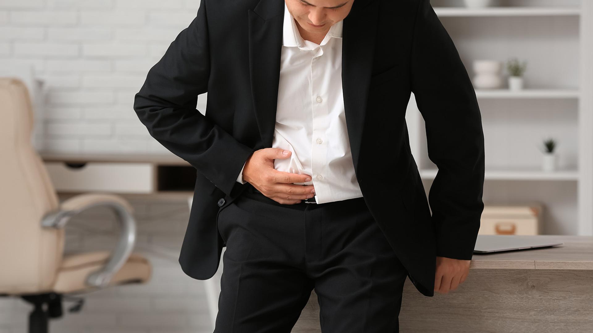 A man in a suit holds his stomach, looking uncomfortable.