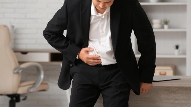 A man in a suit holds his stomach, looking uncomfortable.