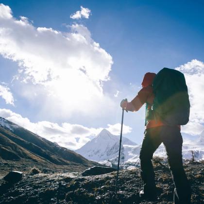 Hiker with backpack trekking in mountainous terrain under a bright sky with clouds