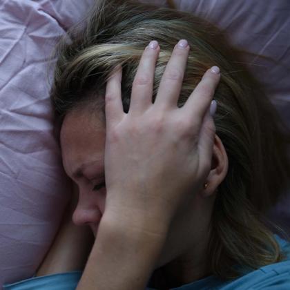 Woman lying down with her hand covering her forehead.
