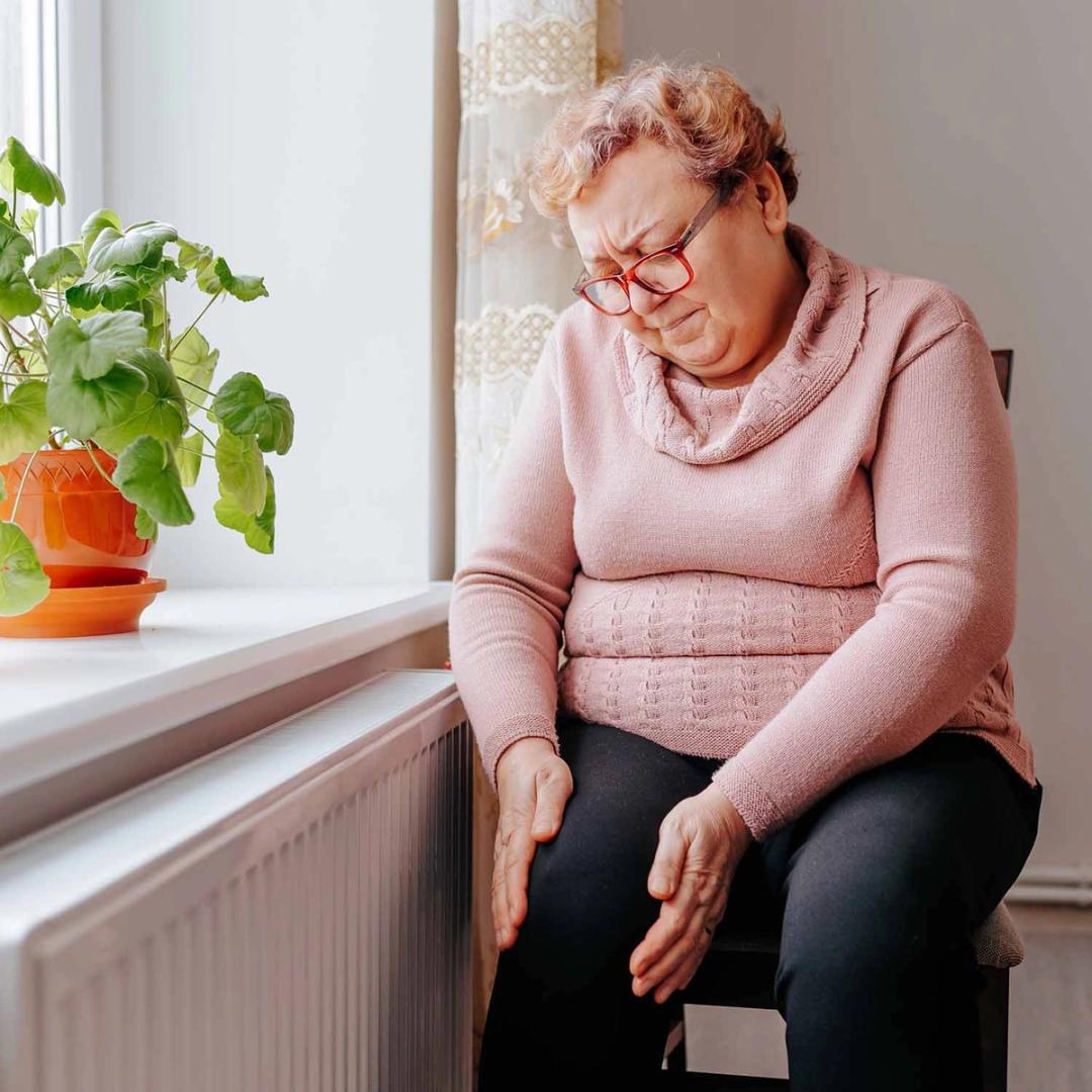 Elderly woman wincing, holding her knees in pain.