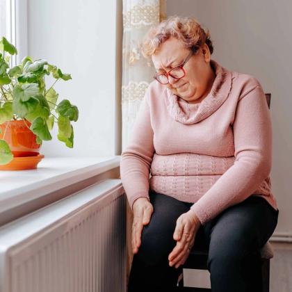 Elderly woman wincing, holding her knees in pain.
