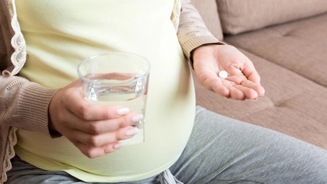A pregnant person holding a glass of water and a white pill.